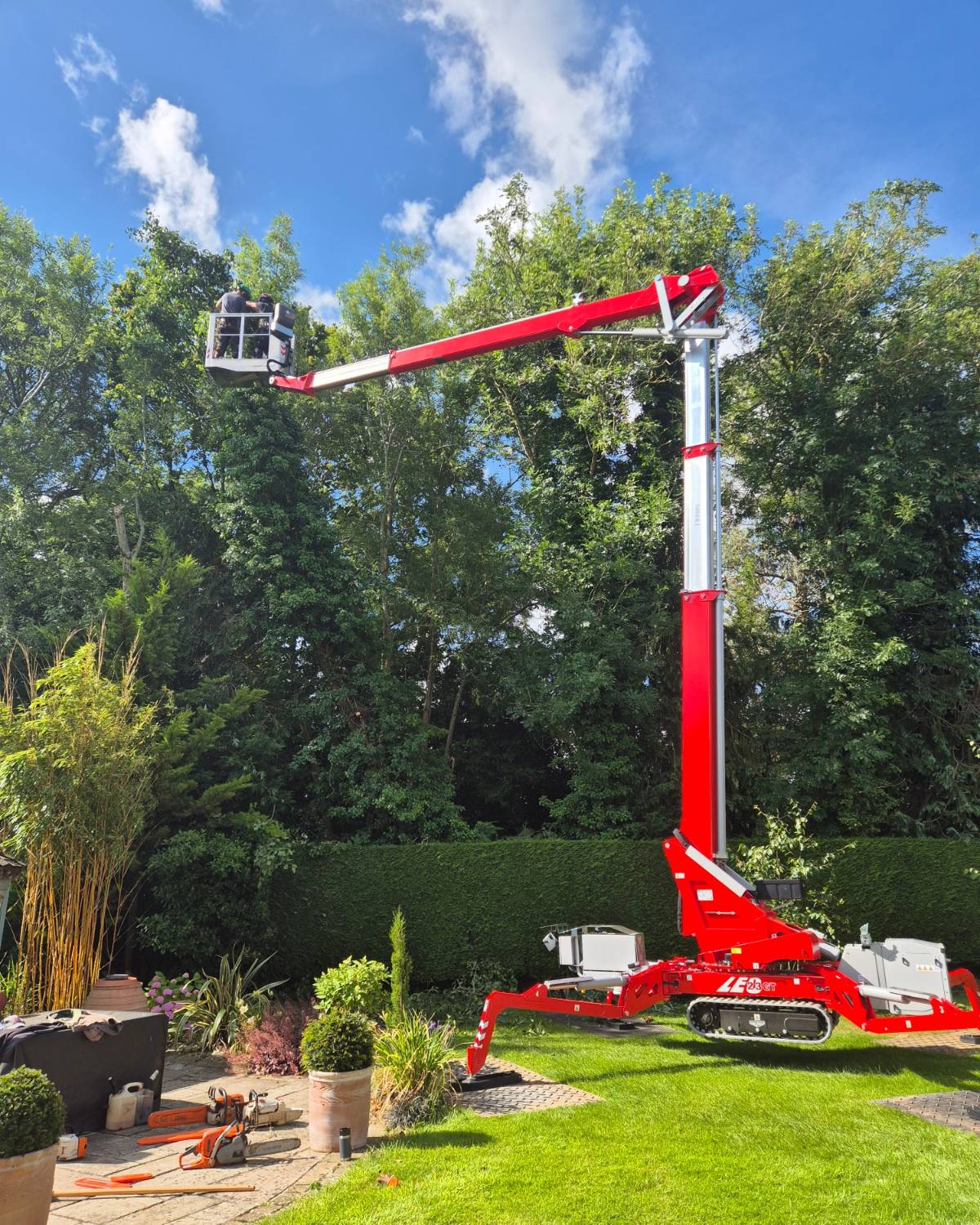 A red tracked spider lift set up in a back garden to reach the trees